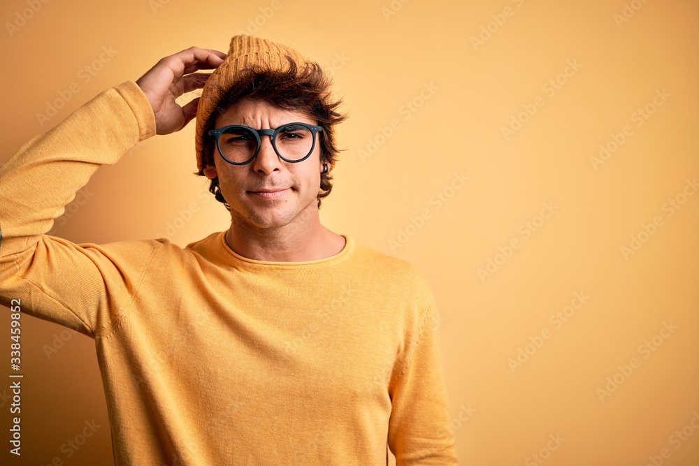 Young handsome man wearing casual t-shirt and glasses over isolated yellow background confuse and wonder about question. Uncertain with doubt, thinking with hand on head. Pensive concept. Young handsome man wearing casual t-shirt and glasses over isolated yellow background confuse and wonder about question. Uncertain with doubt, thinking with hand on head. Pensive concept.