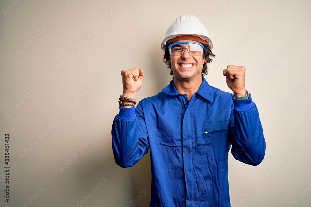 Young constructor man wearing uniform and security helmet over isolated white background celebrating surprised and amazed for success with arms raised and open eyes. Winner concept.