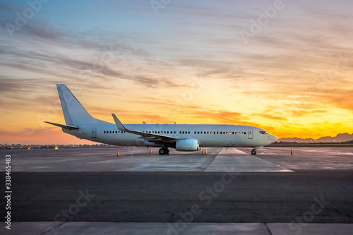 International Airlines Plane Parking Outside The Terminal In The Airport. White Passenger Airplane Side View, Sunset Over The Mountains.