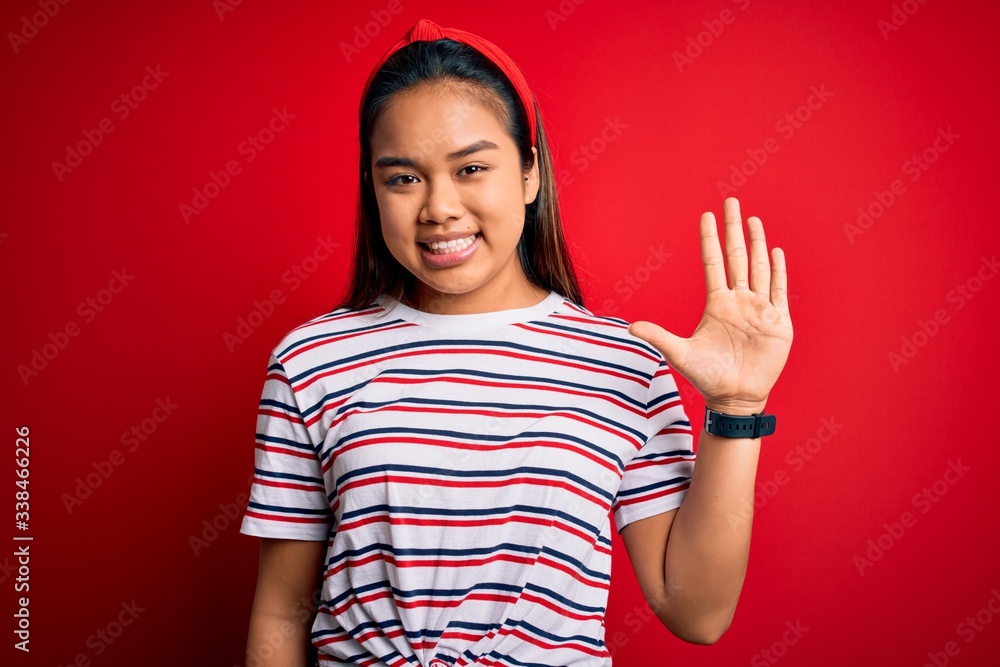 Young beautiful asian girl wearing casual striped t-shirt over isolated red background showing and pointing up with fingers number five while smiling confident and happy. Young beautiful asian girl wearing casual striped t-shirt over isolated red background showing and pointing up with fingers number five while smiling confident and happy.