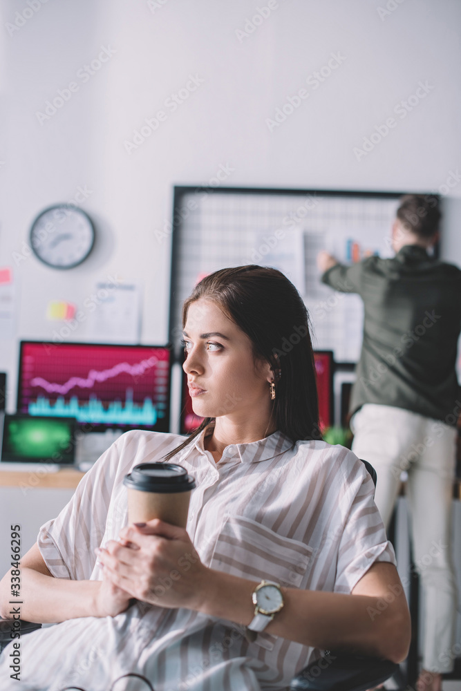 Selective focus of computer systems analyst holding paper cup while colleague in office Selective focus of computer systems analyst holding paper cup while colleague in office