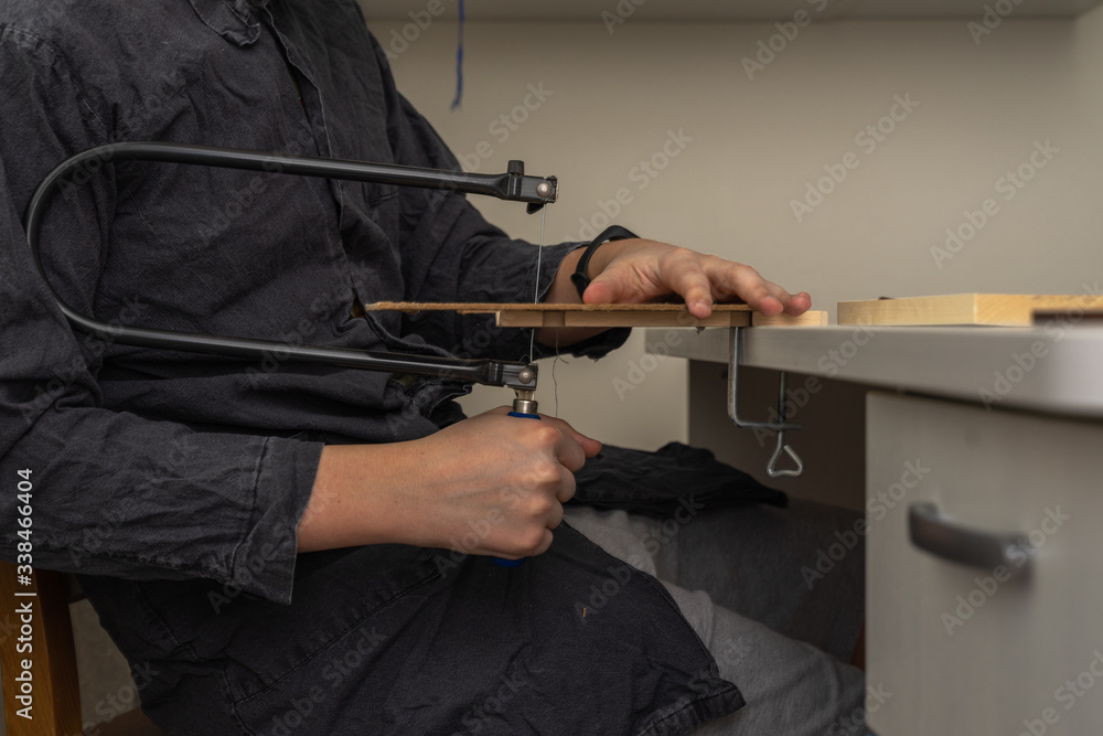a teenager in a work coat sits at a desk engaged in carpentry. activities at home during the period of quarantine and self-isolation