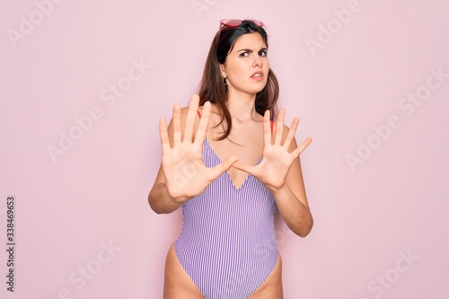 Young beautiful fashion girl wearing swimwear swimsuit and sunglasses over pink background Moving away hands palms showing refusal and denial with afraid and disgusting expression. Stop and forbidden.