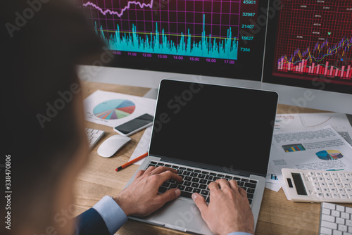Selective focus of data analyst using laptop near charts on papers and computer monitors on table