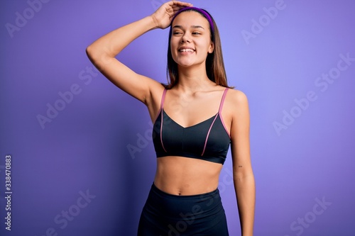 Young beautiful sporty girl doing sport wearing sportswear over isolated purple background smiling confident touching hair with hand up gesture, posing attractive and fashionable © Krakenimages.com