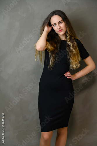 Vertical photo style girl with beautiful long hair in a black dress on a gray background in the studio