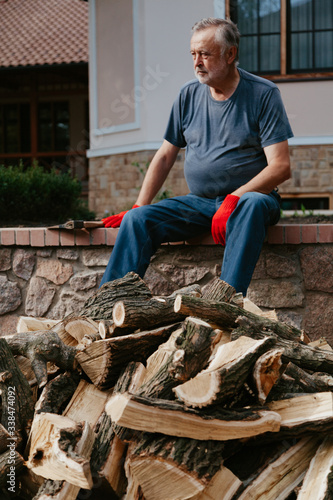 Elderly man in red gloves sits over pile of firewood