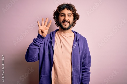 Young handsome sporty man with beard wearing casual sweatshirt over pink background showing and pointing up with fingers number four while smiling confident and happy. © Krakenimages.com