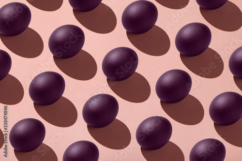 Purple eggs painted for the Easter holiday on a pink background with a hard shadow, pattern on the background, space for text