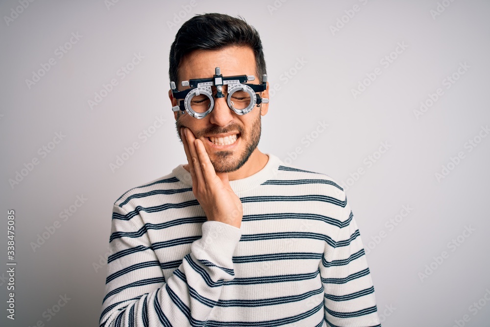 Young handsome man with beard wearing optometry glasses over isolated white background touching mouth with hand with painful expression because of toothache or dental illness on teeth. Dentist Young handsome man with beard wearing optometry glasses over isolated white background touching mouth with hand with painful expression because of toothache or dental illness on teeth. Dentist