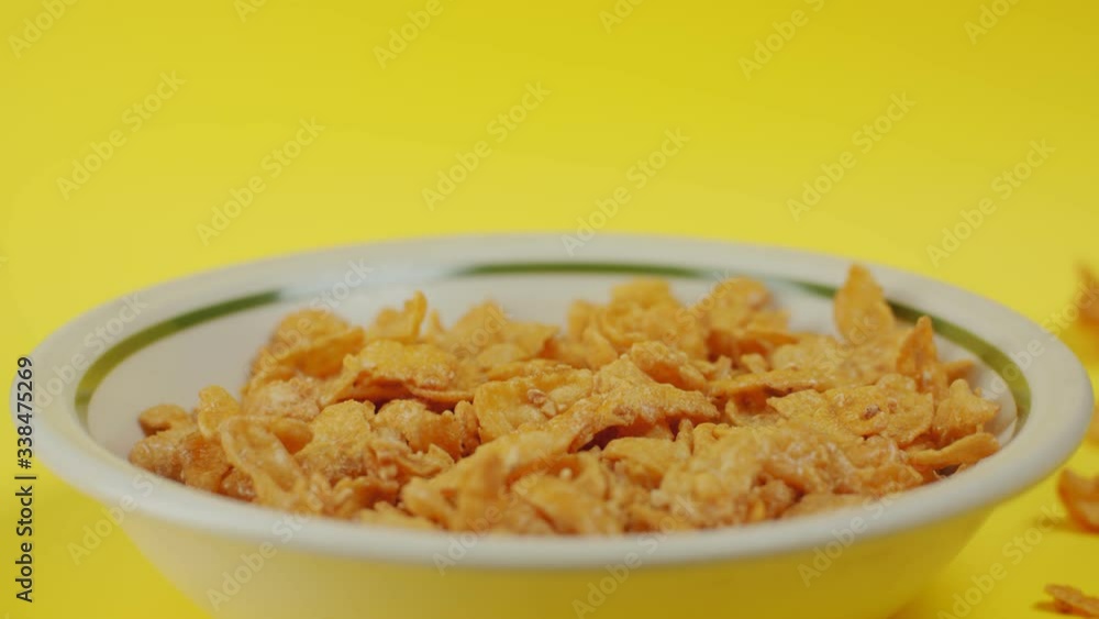 A 4K close up shot, side view, of cereal // corn flakes // crunchy nut being poured into a bowl. Slow motion shot of cereal dropping from the sky into a bowl. Bowl on yellow A 4K close up shot, side view, of cereal // corn flakes // crunchy nut being poured into a bowl. Slow motion shot of cereal dropping from the sky into a bowl. Bowl on yellow