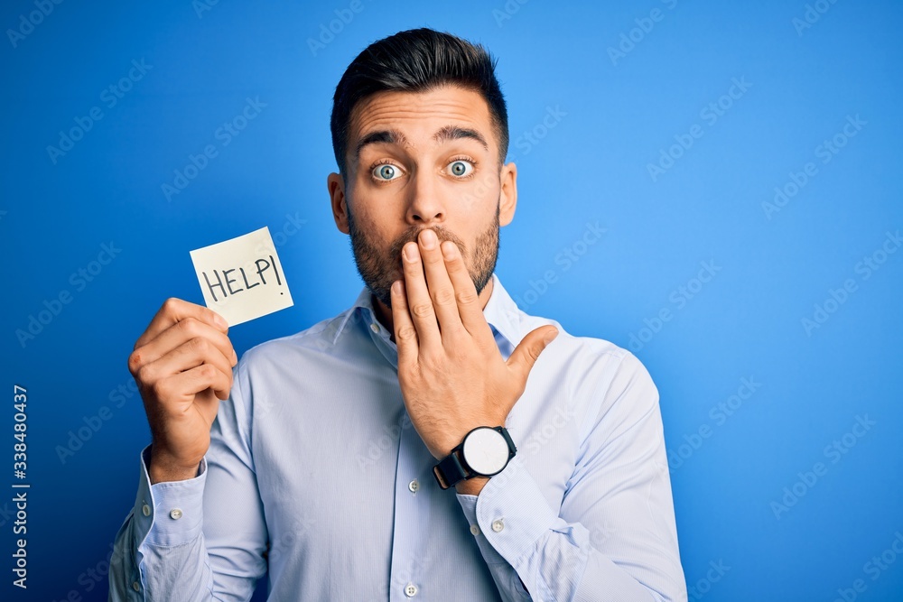 Young overworked business man asking for help holding paper over blue background cover mouth with hand shocked with shame for mistake, expression of fear, scared in silence, secret concept Young overworked business man asking for help holding paper over blue background cover mouth with hand shocked with shame for mistake, expression of fear, scared in silence, secret concept