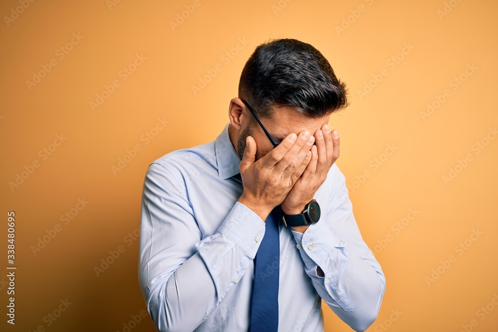 Young handsome businessman wearing tie and glasses standing over yellow background with sad expression covering face with hands while crying. Depression concept. Young handsome businessman wearing tie and glasses standing over yellow background with sad expression covering face with hands while crying. Depression concept.
