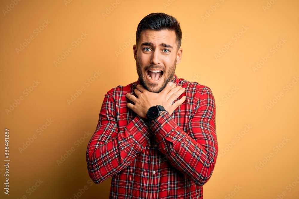Fototapeta premium Young handsome man wearing casual shirt standing over isolated yellow background shouting and suffocate because painful strangle. Health problem. Asphyxiate and suicide concept.