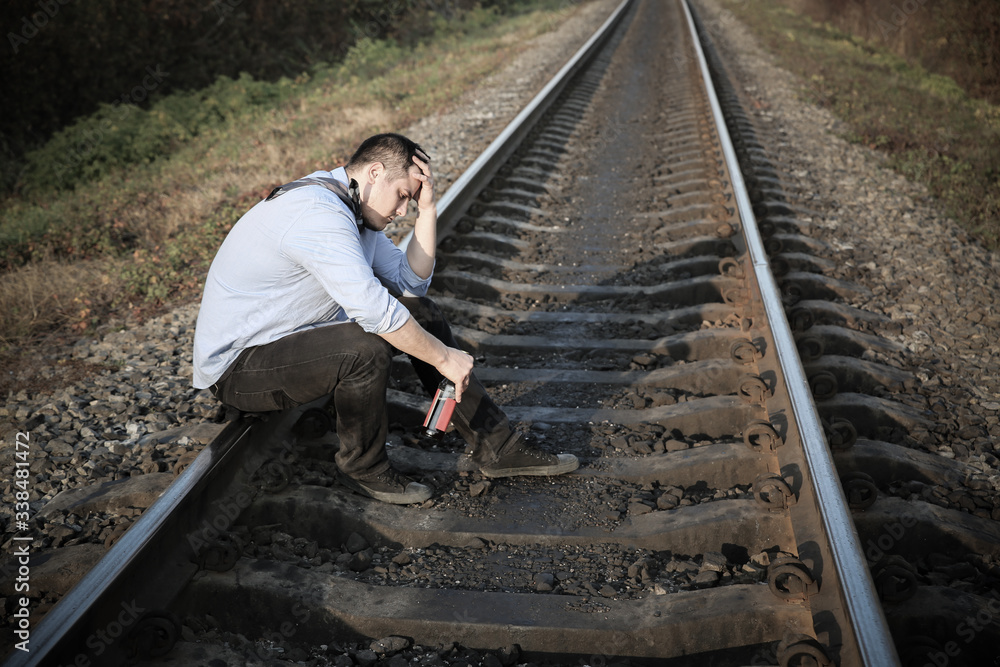 Fototapeta premium Man with alcohol on railway tracks outdoors. Depression disease. Economy crisis, poverty, unemployment concept. Consequences of coronavirus people isolation during quarantine. Hopelessness.