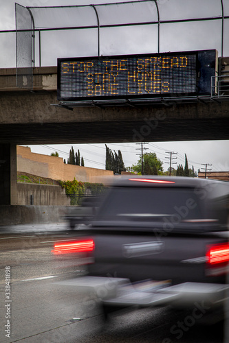 Government digital freeeway sign at overpass with message stating “Stop The Spread ,Stay Home, Save Lives” and traffic blurred under the sign during the Coronavirus Pandemic photo