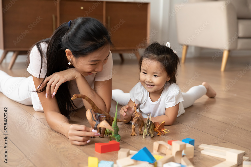 Lying on warm wooden floor asian mom play game with little daughter holds dinosaurs toys heap of colorful construction blocks nearby. Spend time have fun together educational activity with kid concept Lying on warm wooden floor asian mom play game with little daughter holds dinosaurs toys heap of colorful construction blocks nearby. Spend time have fun together educational activity with kid concept