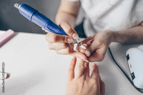 Hardware professional manicure process  cleaning of nails by a milling cutter. Close up female hands in beauty salon. Finger nail treatment  making process. Electric nail file drill in action