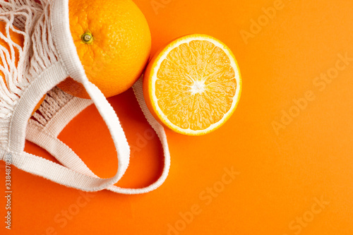 Cutting orange in cotton shopping eco friendly bag on orange background. Citrus harvest, monochrome composition