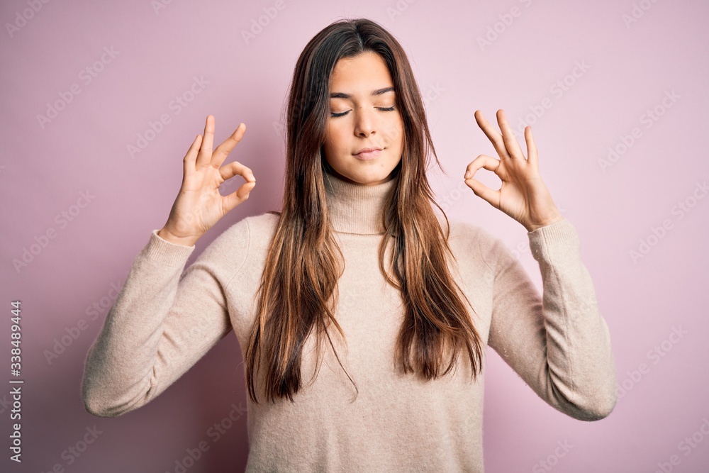Young beautiful girl wearing casual turtleneck sweater standing over isolated pink background relax and smiling with eyes closed doing meditation gesture with fingers. Yoga concept. Young beautiful girl wearing casual turtleneck sweater standing over isolated pink background relax and smiling with eyes closed doing meditation gesture with fingers. Yoga concept.