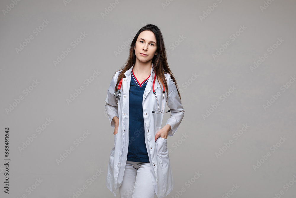 Stock photo of a professional brunette doctor or nurse or physician wearing white lab coat with stethoscope looking at camera, holding her hands in pockets. Stock photo of a professional brunette doctor or nurse or physician wearing white lab coat with stethoscope looking at camera, holding her hands in pockets.