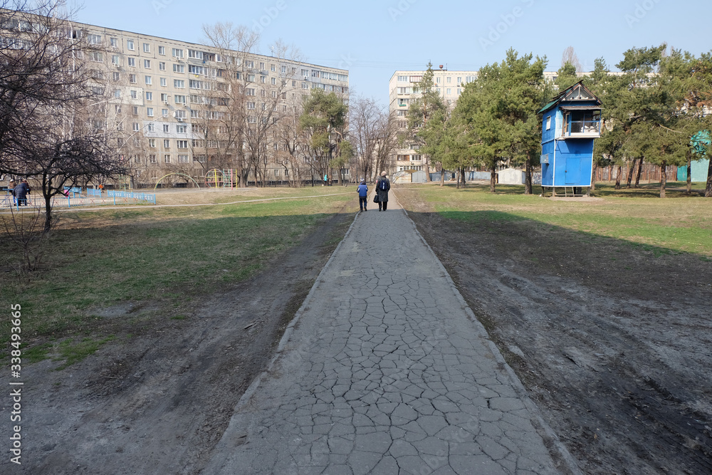 A wide dry asphalt road with woman and little boy, standing on the end of shadow, created by sun. Typical ukrainian buildings around in the capital of Ukraine - Kyiv, spring time
