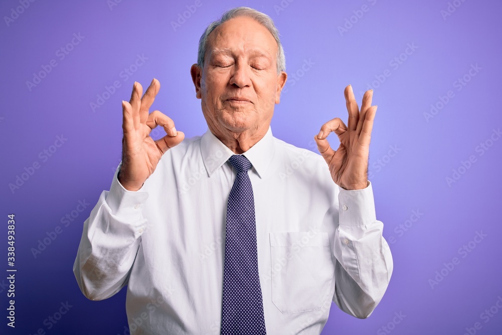 Grey haired senior business elegant man standing over purple isolated background relax and smiling with eyes closed doing meditation gesture with fingers. Yoga concept. Grey haired senior business elegant man standing over purple isolated background relax and smiling with eyes closed doing meditation gesture with fingers. Yoga concept.