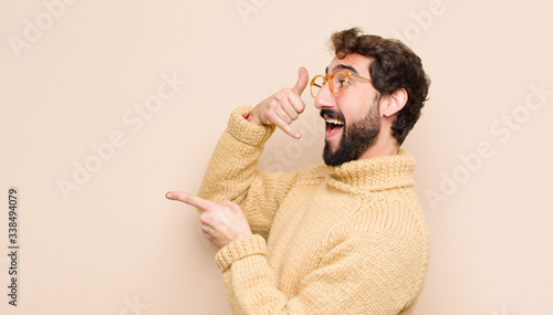 Tableau sur toile young cool man smiling cheerfully and pointing to camera while making a call you