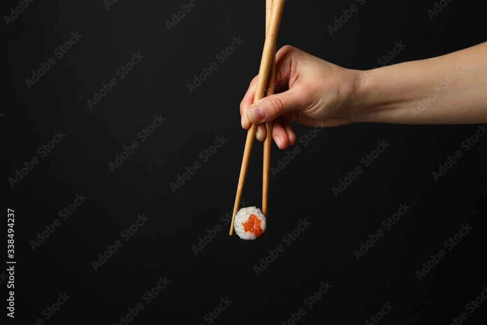 Fototapeta premium Female hand with chopsticks hold sushi roll on black background. Japanese food
