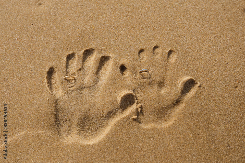Two left handprints on the sand with wedding rings on the summer beach. Newlyweds hands shapes. Concept of honeymoon Two left handprints on the sand with wedding rings on the summer beach. Newlyweds hands shapes. Concept of honeymoon