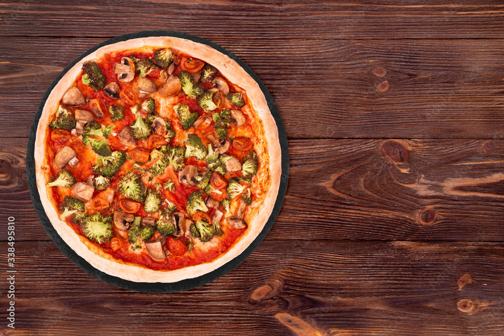 Pizza with veggie vegetables on slate bottom, on wooden table top view, space for text Pizza with veggie vegetables on slate bottom, on wooden table top view, space for text