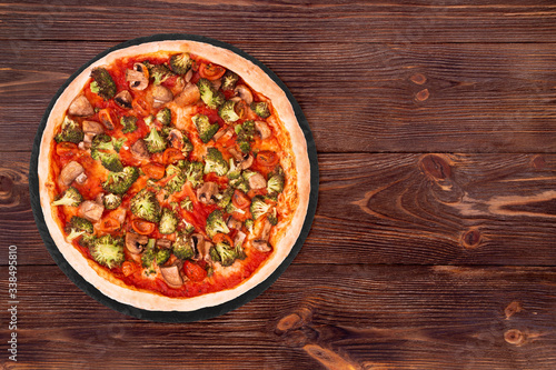 Pizza with veggie vegetables on slate bottom, on wooden table top view, space for text