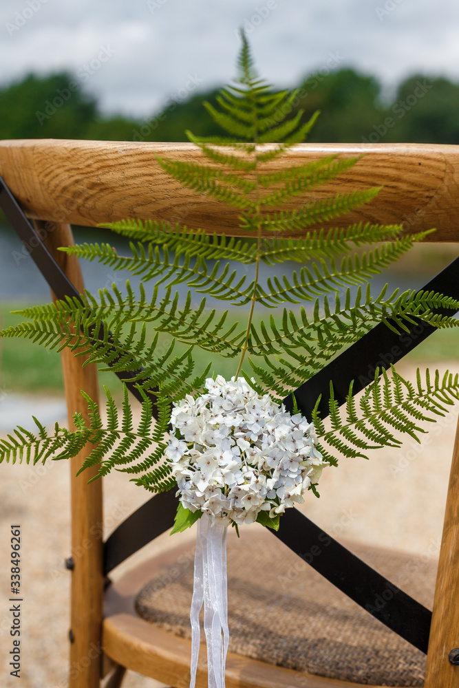 Wooden chair for guests decorated with fern branch,  flowers and ribbons in rustic style . Wedding ceremony decor