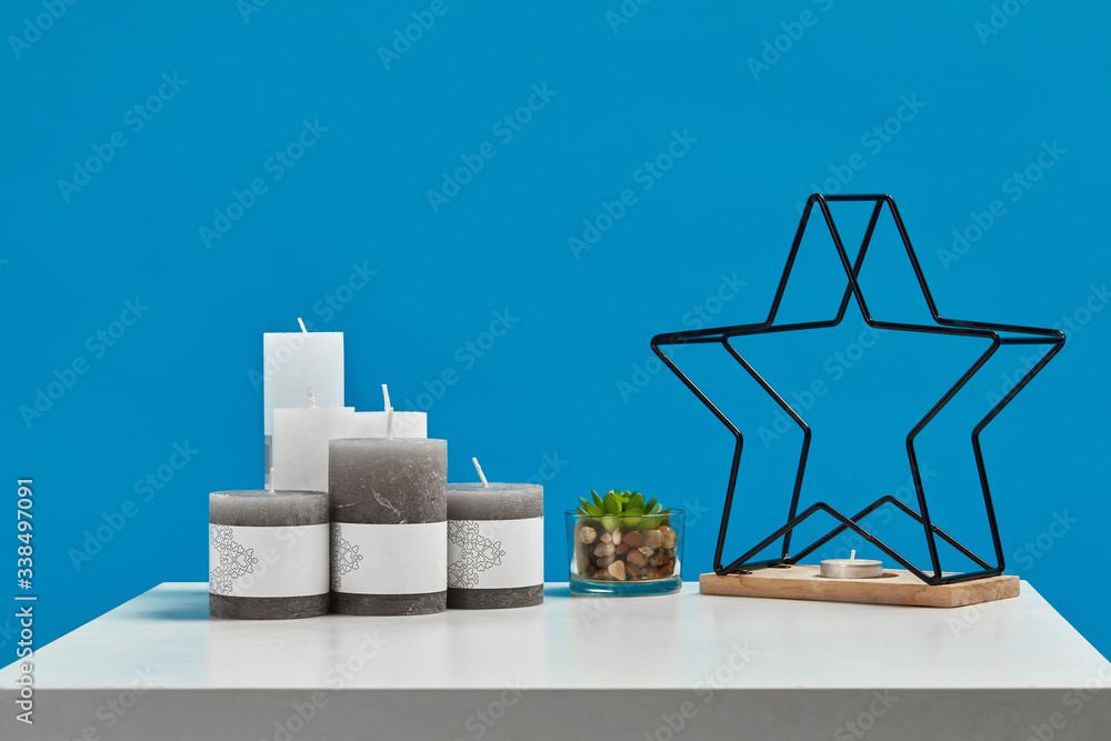 White table with green succulent, some candles with copy space, candlestick in form of black iron star on wooden stand. Blue background. Close up