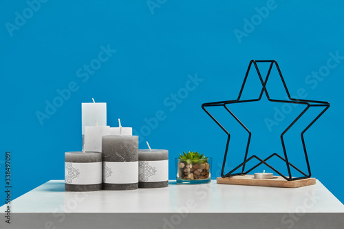 White table with green succulent, some candles with copy space, candlestick in form of black iron star on wooden stand. Blue background. Close up