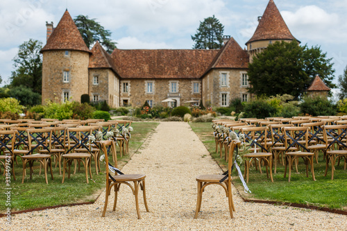 Wedding ceremony on the background of old castle. Rows of wooden chairs for guests standing on the grass in garden of France chateau. Beautiful area for open-air celebration