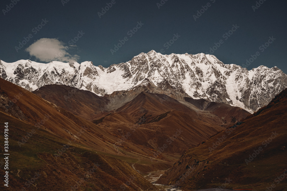 landscape of snow-capped mountain peaks and sunny valley in autumn