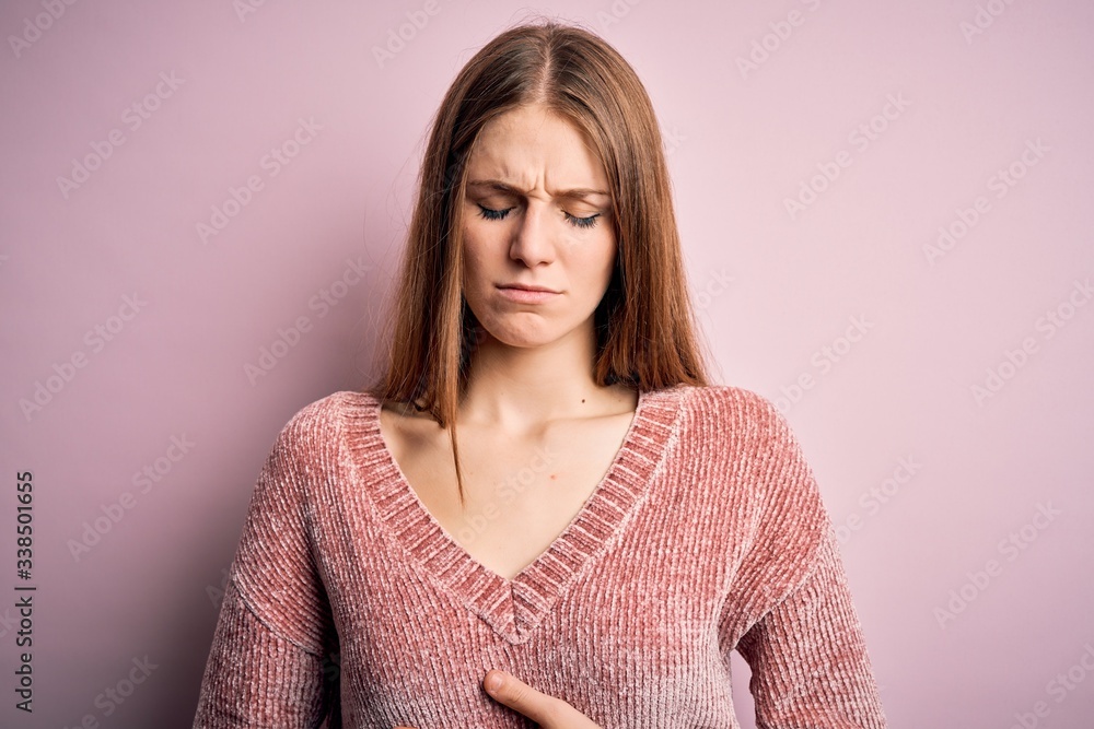 Fototapeta premium Young beautiful redhead woman wearing casual sweater over isolated pink background with hand on stomach because indigestion, painful illness feeling unwell. Ache concept.
