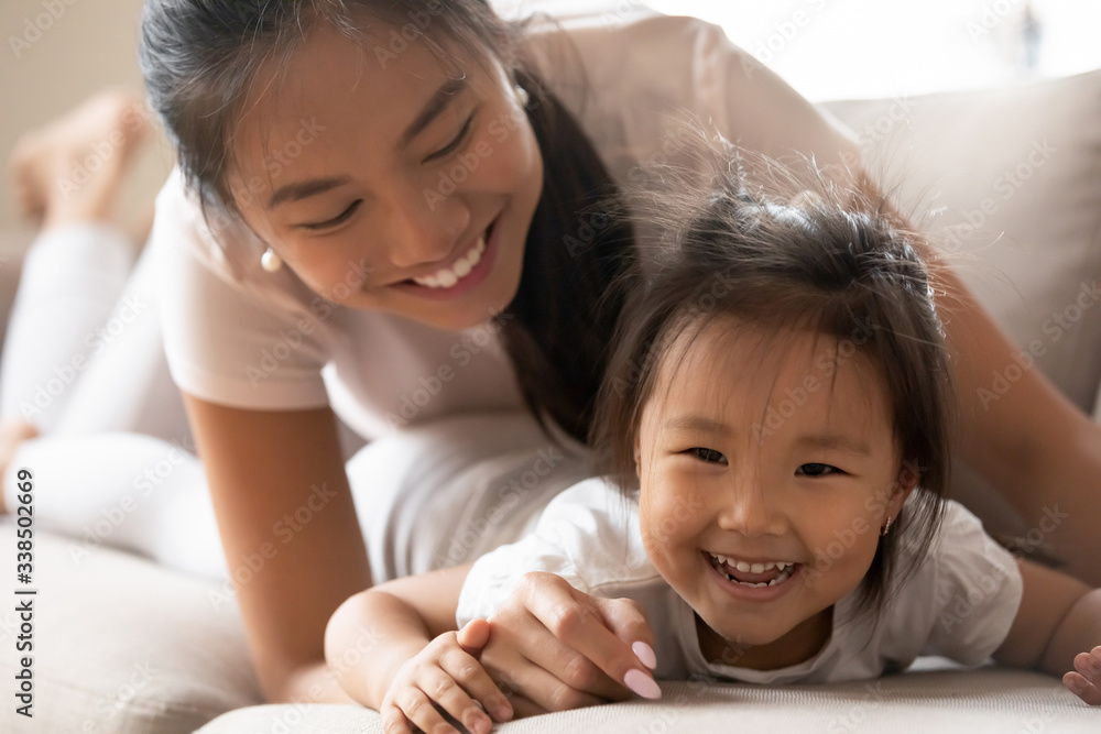 Close up image, Asian toddler kid girl spending active funny time with mother or babysitter at home. Lying on couch in living room mom laughing relish weekend activity with adorable little daughter Close up image, Asian toddler kid girl spending active funny time with mother or babysitter at home. Lying on couch in living room mom laughing relish weekend activity with adorable little daughter
