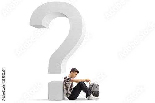 Sad male student sitting on the floor and leaning against a que‪stion mark photo