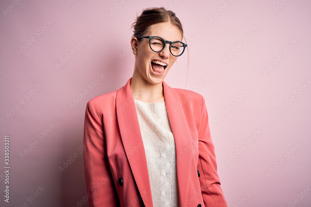 Young beautiful redhead woman wearing jacket and glasses over isolated pink background winking looking at the camera with sexy expression, cheerful and happy face.