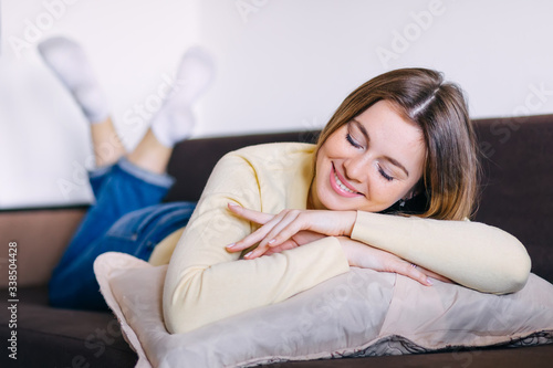 Attractive young woman lying on a sofa with her chin resting on her arms, eyes closed and a smile of pleasure on face