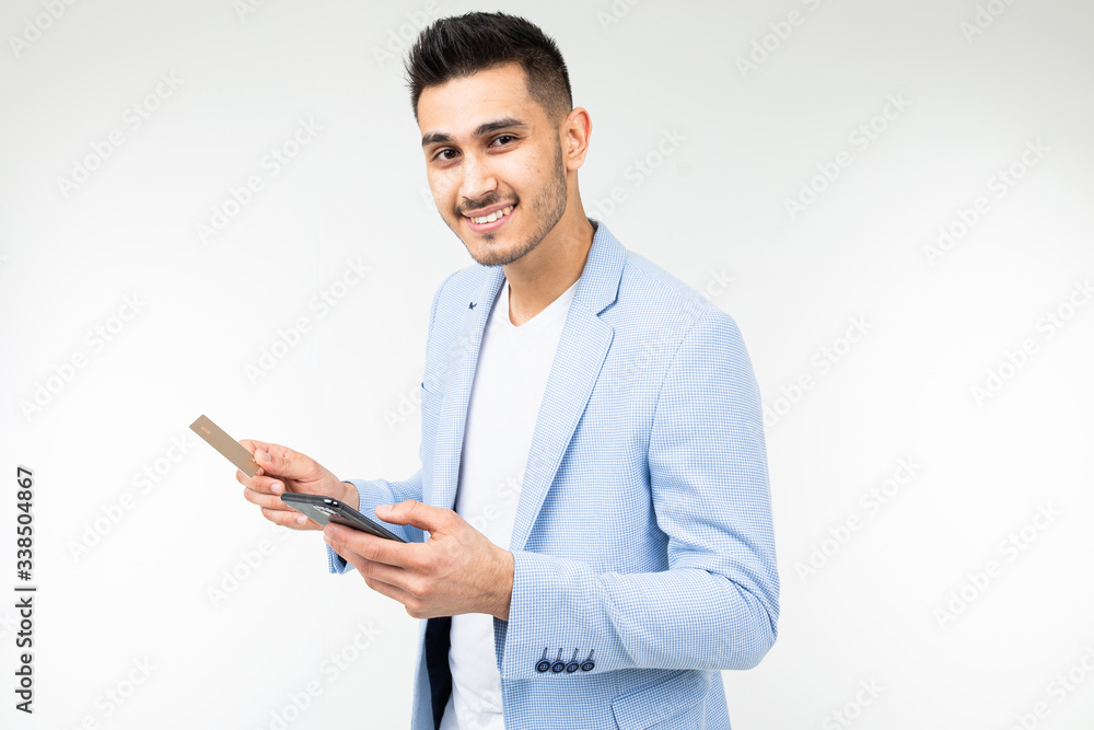 handsome man in a jacket orders purchases via the Internet from a smartphone holding a credit card in his hands handsome man in a jacket orders purchases via the Internet from a smartphone holding a credit card in his hands