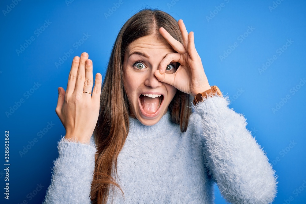 Young beautiful redhead woman wearing wedding ring on finger over blue background with happy face smiling doing ok sign with hand on eye looking through fingers Young beautiful redhead woman wearing wedding ring on finger over blue background with happy face smiling doing ok sign with hand on eye looking through fingers