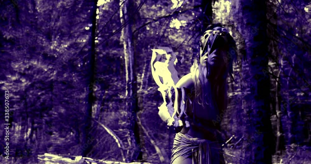 wild woman with bird skull mask and flaming stick in hand is sneaking through woodland