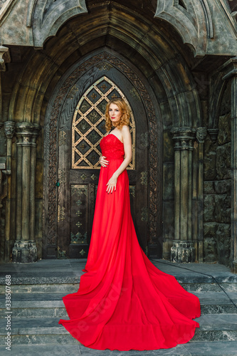 A woman in a red dress stands on a background of a medieval castle