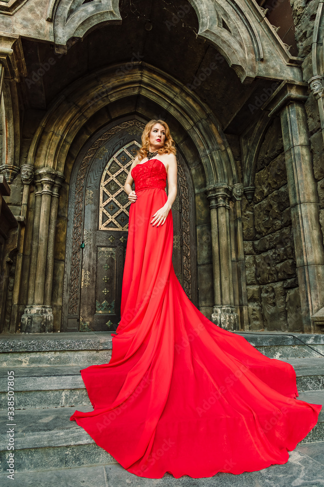 Naklejka premium A woman in a red dress stands on a background of a medieval castle