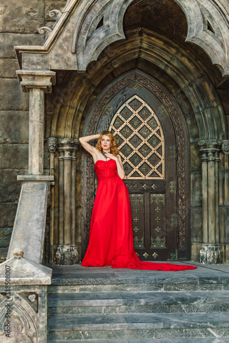 A woman in a red dress stands on a background of a medieval castle