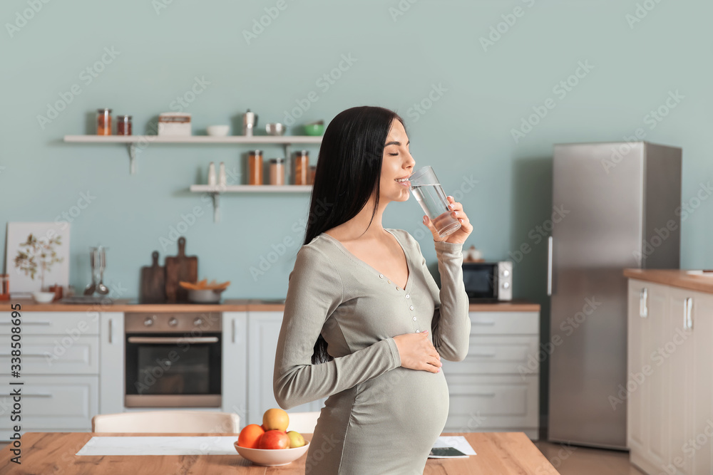 Beautiful pregnant woman drinking water in kitchen Beautiful pregnant woman drinking water in kitchen
