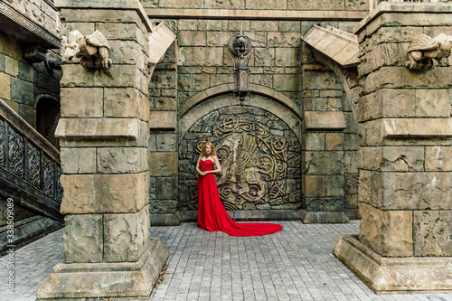 A woman in a red dress stands on a background of a medieval castle